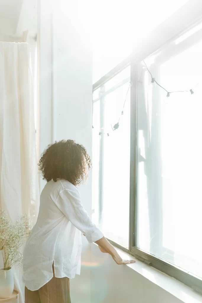 A woman looking out the window and practicing coping methods for anxiety.